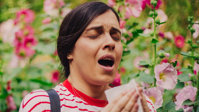 woman sneezing with allergies in a flower patch