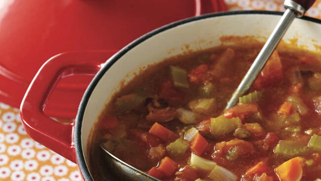 autumn garden soup with carrots, onions, tomatoes, and celery in a red enameled dutch oven