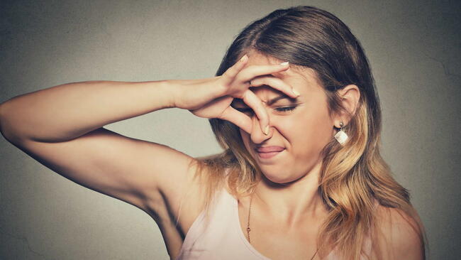 Closeup portrait headshot woman pinches nose with fingers hands looks with disgust something stinks bad smell situation isolated on gray wall background. Human face expression body language reaction