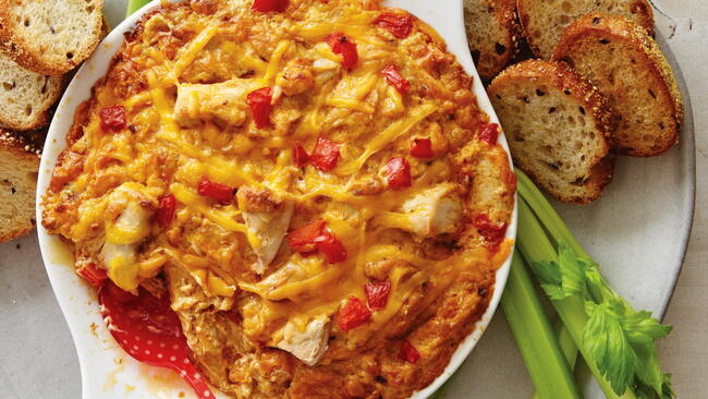 A white dish of buffalo chicken and cheese dip, surrounded by bread slices