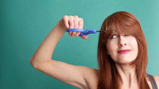 woman cutting her own hair to save money