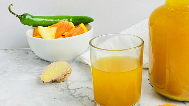 Glass of homemade fire cider with ginger, chili pepper, citrus slices, and apple cider vinegar
