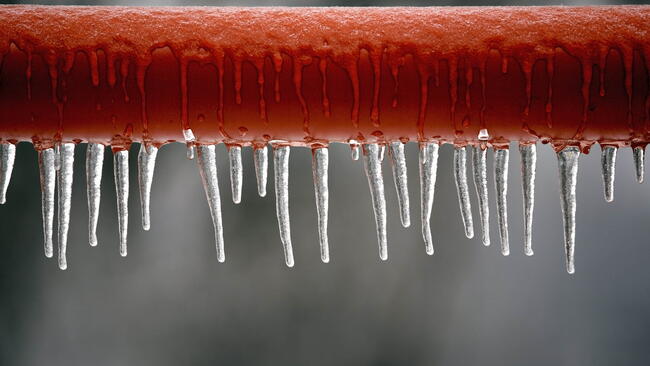 Icicles hanging from a brown pipe. Frozen water and metal surface, winter time concept. selective focus shallow depth of field. frozen pipes