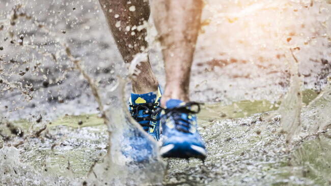 Trail runner man walking in a puddle, splashing his shoes. Cross country trail