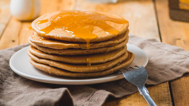 a stack of Pancakes from rye flour with syrup on top on a plate with a fork