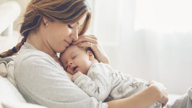 A mother cradles a sleeping baby while lying down 