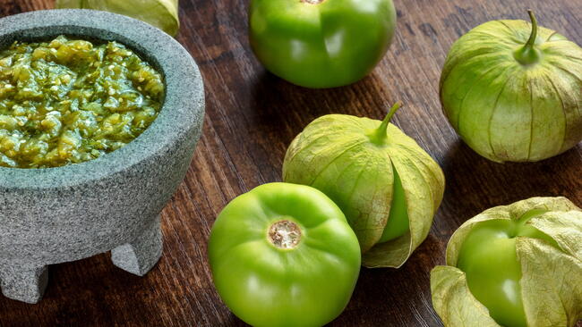 Green tomatoes next to a bowl of salsa verde