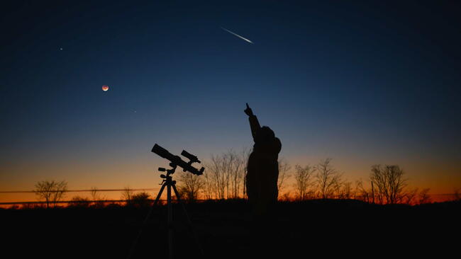 Astronomer looking at the starry skies and crescent Moon with a telescope.