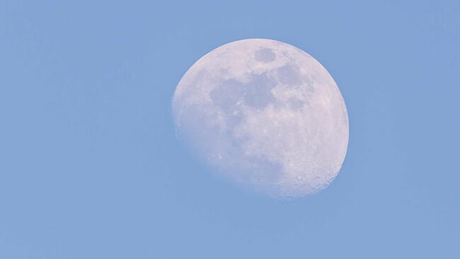 Horizontal photo of white big moon. Moon is captured during a day time with clear blue sky and few days before full-moon so only small part is hidden in shadow of Earth.