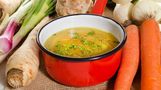 Vegetable stock in a red pot, surrounded by vegetables