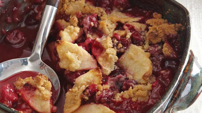 closeup of serving spoon dipping into pan of apple cranberry crisp