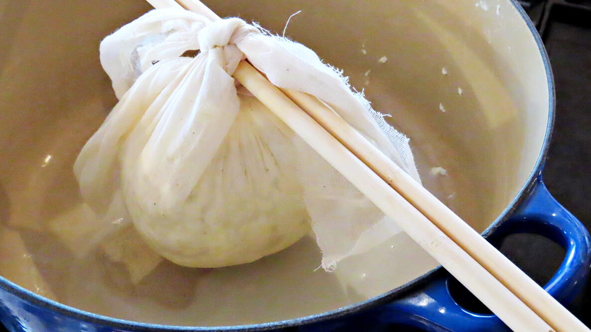 A bag of cheese hanging on chopsticks over a bowl 