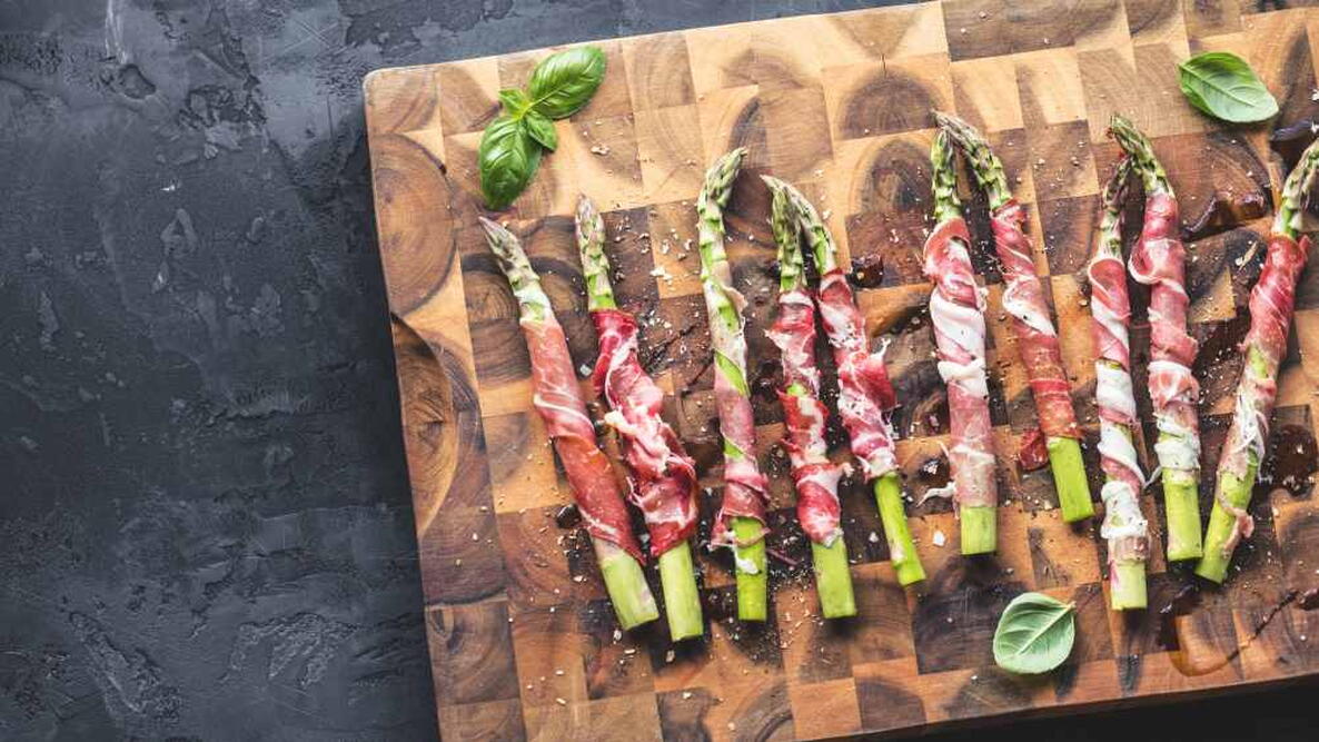 top view of fresh organic asparagus wrapped in parma ham on wooden surface