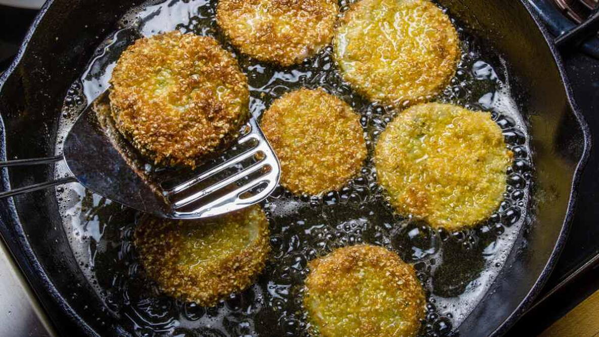 Slices of green tomato being fried in a cast iron skillet to make fried green tomatoes