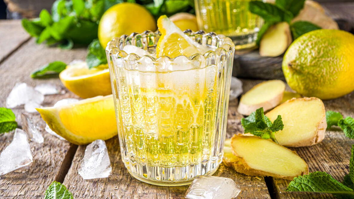 Homemade ginger lemonade cocktail. Cold summer ginger lemon ale. Sweet and sour iced refreshing beverage with lemon slice garnish, Detox and weight loss drink. Wooden rustic background