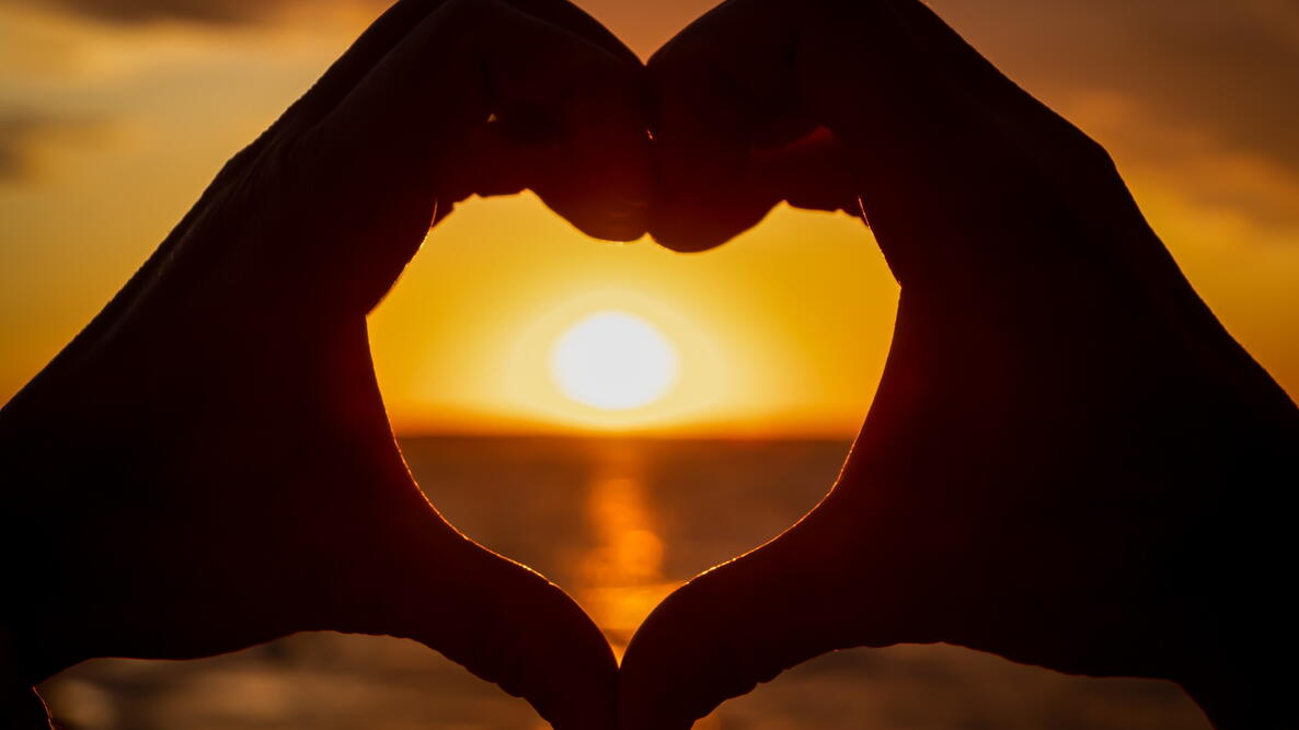 two hands making a heart to frame the sun