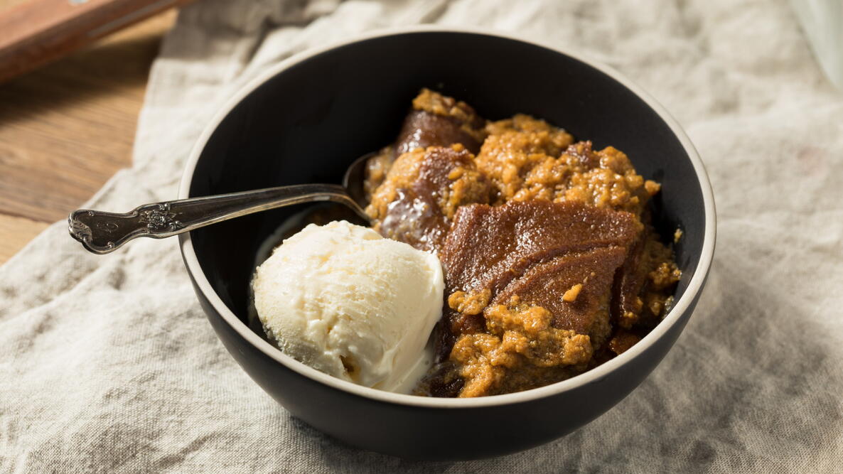 traditional cornmeal indian pudding in a bowl with a spoon and a scoop of vanilla ice cream