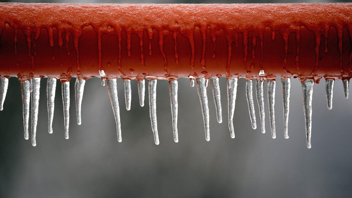Icicles hanging from a brown pipe. Frozen water and metal surface, winter time concept. selective focus shallow depth of field. frozen pipes