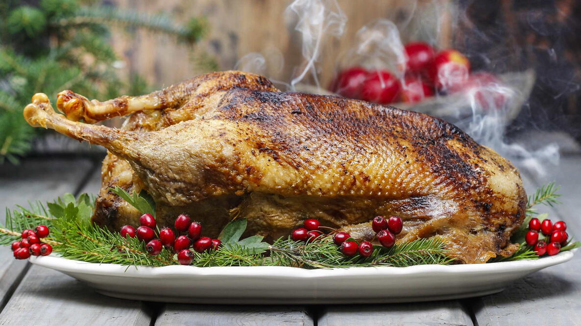 roast goose on the holiday table, on a platter with cranberries and festive herbs