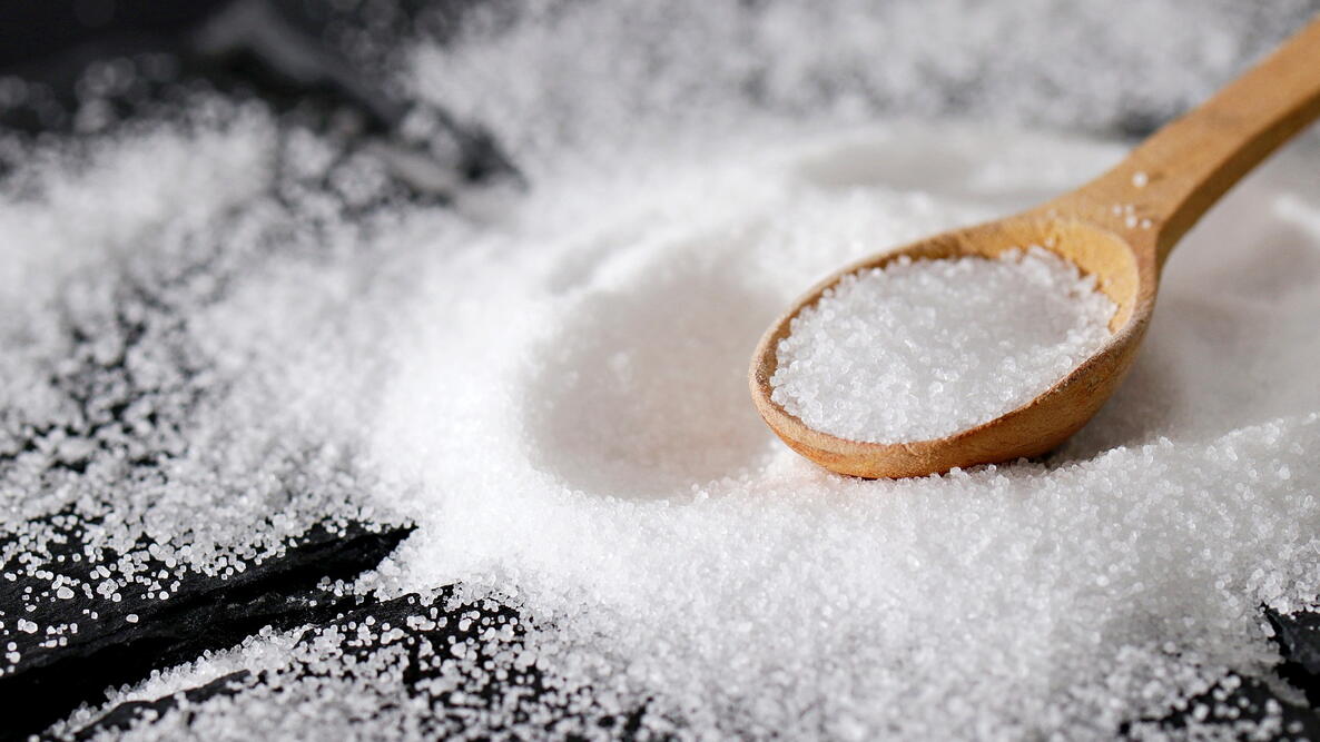 Close-up of salt on a black table, with a full wooden spoon