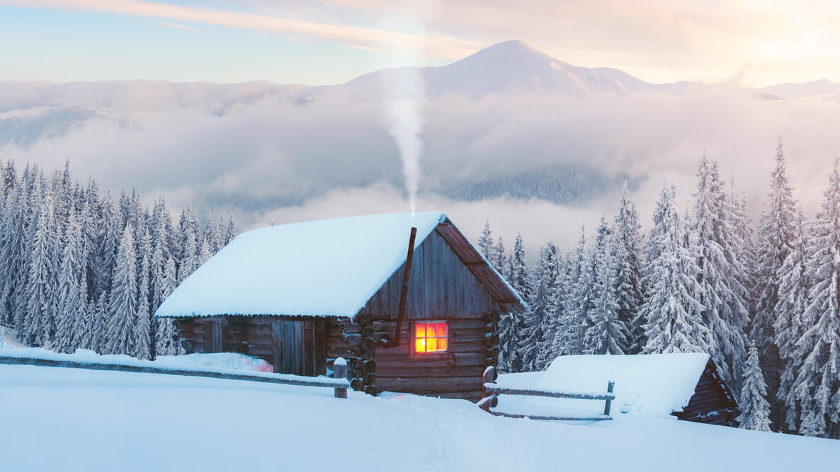 Fantastic winter landscape with wooden house in snowy mountains. Smoke comes from the chimney of snow covered hut. Christmas holiday and winter vacations concept
