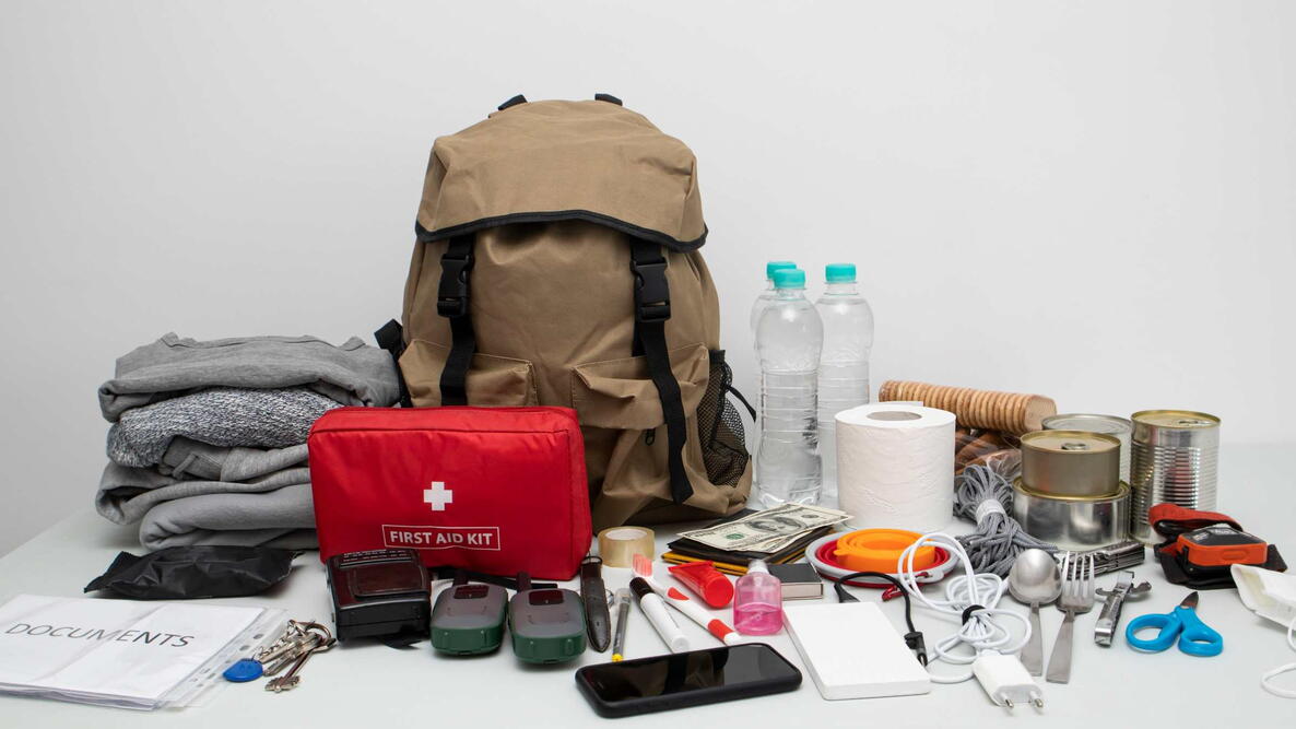 Emergency backpack equipment organized on the table. Documents, water,food, first aid kit and another items needed to survive.
