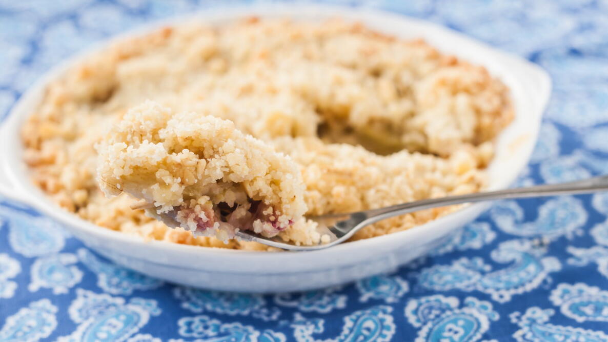 crumble with rhubarb and apple in a bowl on a blue tablecloth with a spoon