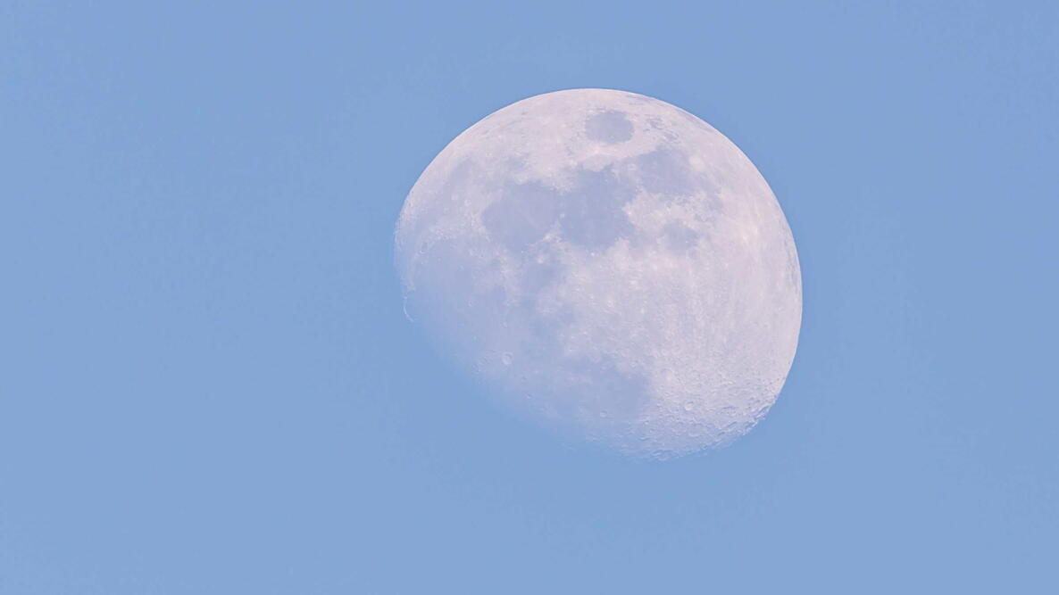 Horizontal photo of white big moon. Moon is captured during a day time with clear blue sky and few days before full-moon so only small part is hidden in shadow of Earth.
