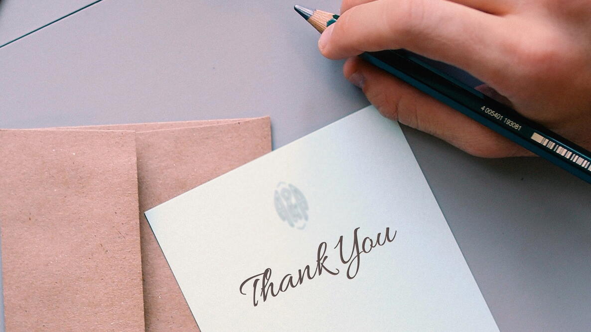 A hand holding a pencil above a note saying "Thank You"