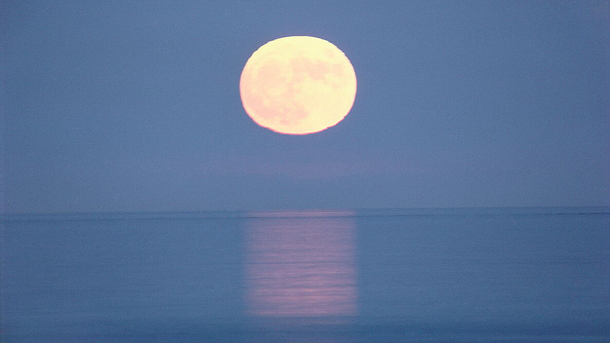 the Moon shining over the ocean with a reflection