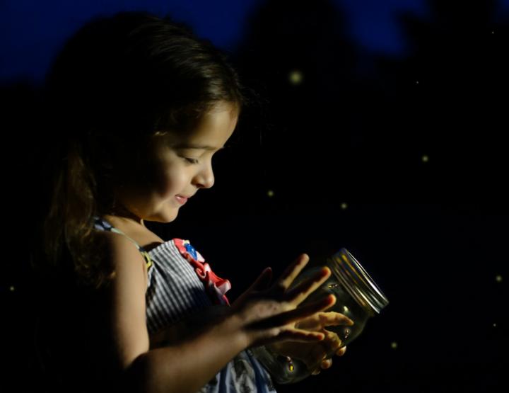 a girl holding a firefly in a mason jar