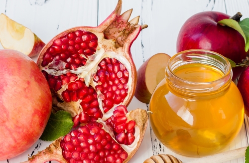 pomegranate, honey and apples on a white table