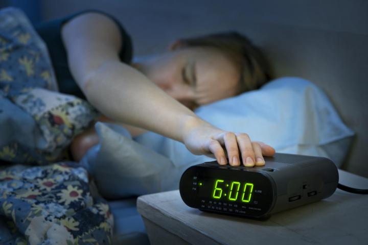 woman sleeping and hitting an alarm clock in the morning